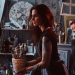 Young attractive painter is holdind jar with brushes in her own cozy workshop